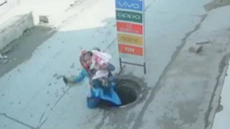 Mulher cai em bueiro com a filha no colo ao seu distrair com seu celular - Foto: Reprodução / YouTube